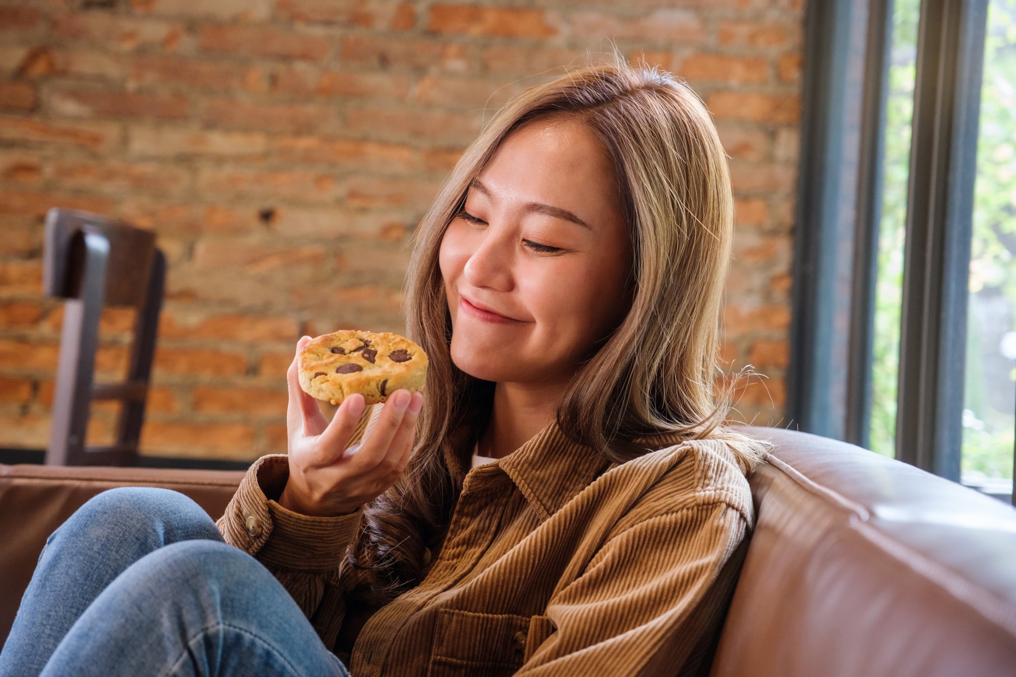 Portrait image of a beautiful young asian woman holding and eating a piece of cookie