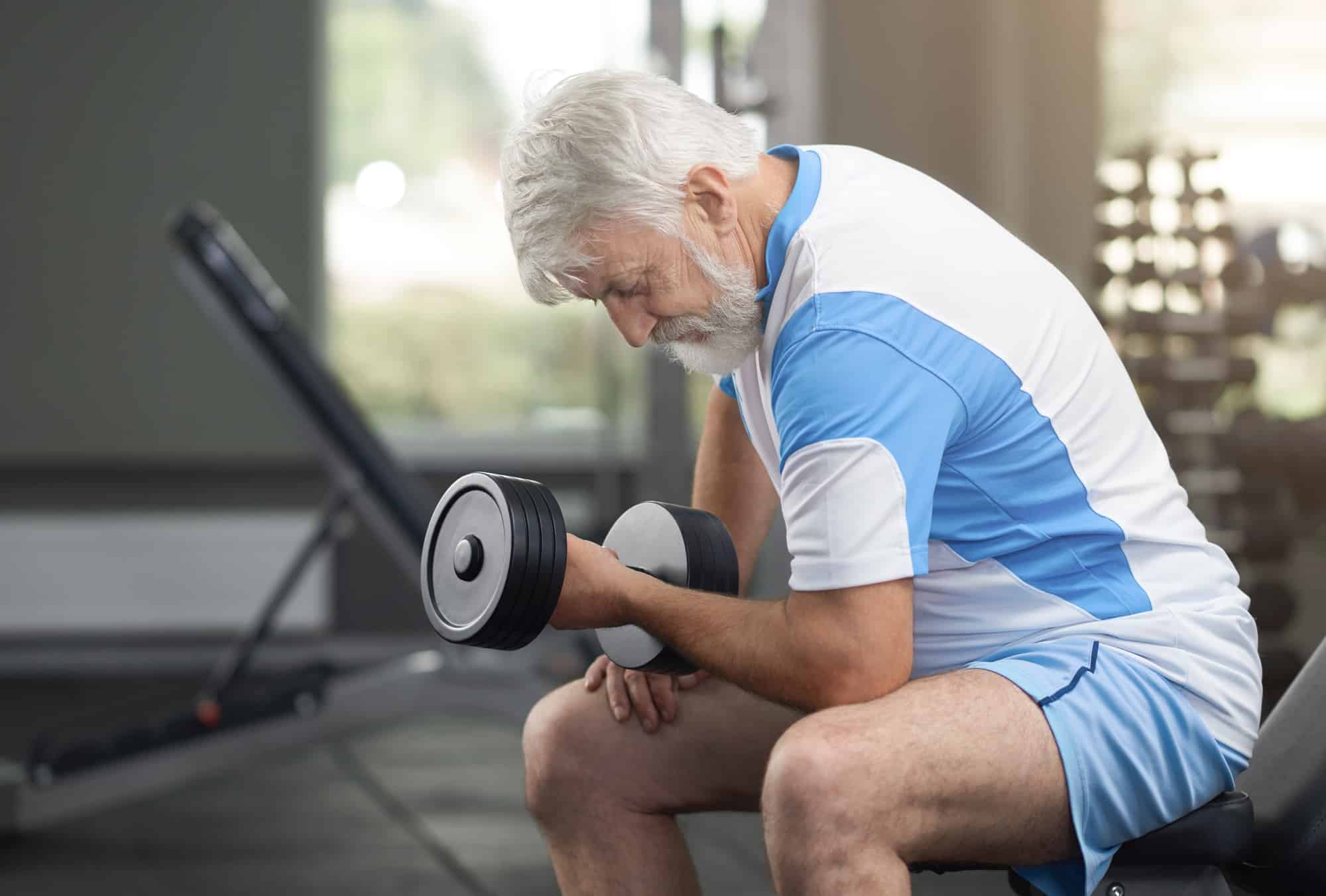 Fit elderly man strength training with dumbbells in gym